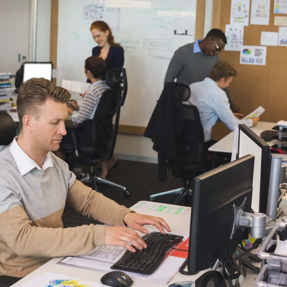 Businessman typing on keyboard while colleagues working in background